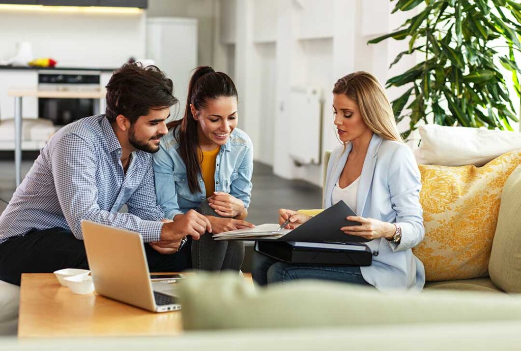 A smiling young adult holding papers and discussing insurance options with a trusted friend at a desk in a home setting. KEYWORDS: ["young adult life insurance","financial planning","local insurance decisions"]